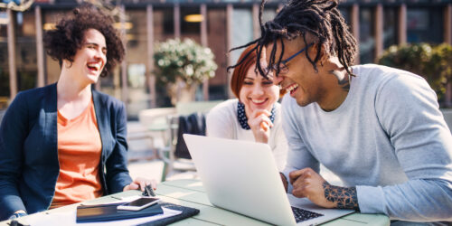 Diverse HR team laughing and collaborating outdoors with a laptop