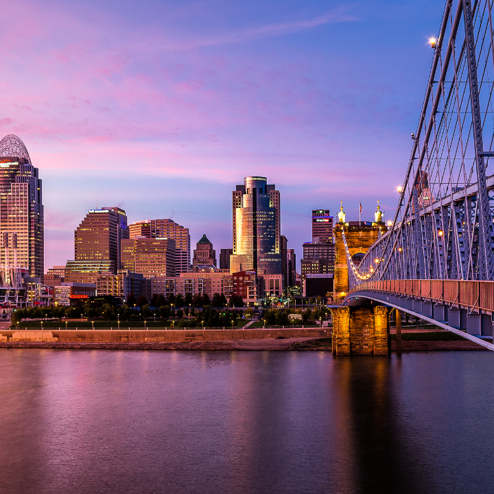 A vibrant view of the Cincinnati skyline at dusk, featuring the John A. Roebling Suspension Bridge and illuminated downtown buildings, highlighting the city served by top staffing agency Cincinnati professionals.