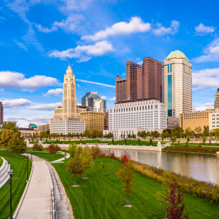 A clear daytime view of downtown Columbus, Ohio, with skyscrapers rising above the riverfront park and a winding path—capturing the city served by trusted temp consultants in Columbus.