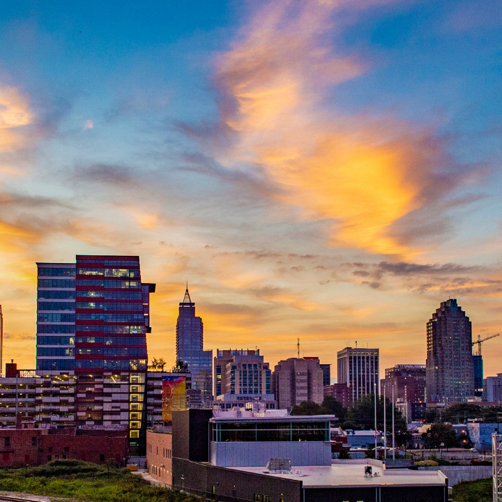 A colorful sunset over the Raleigh, NC skyline, featuring modern office buildings and high-rises—symbolizing the region’s innovation and the presence of Raleigh-Durham temp workforce experts.