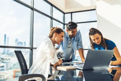Three coworkers collaborate around a laptop, illustrating how MSP and VMS support positive workforce outcomes for midsize companies